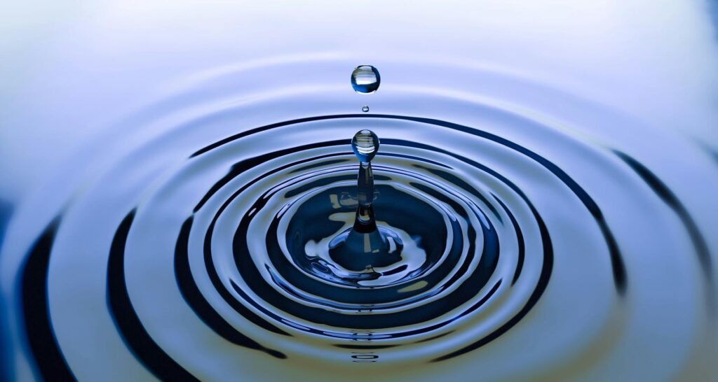 A stunning close-up of a water droplet creating ripples on a smooth water surface, capturing nature's simplicity.